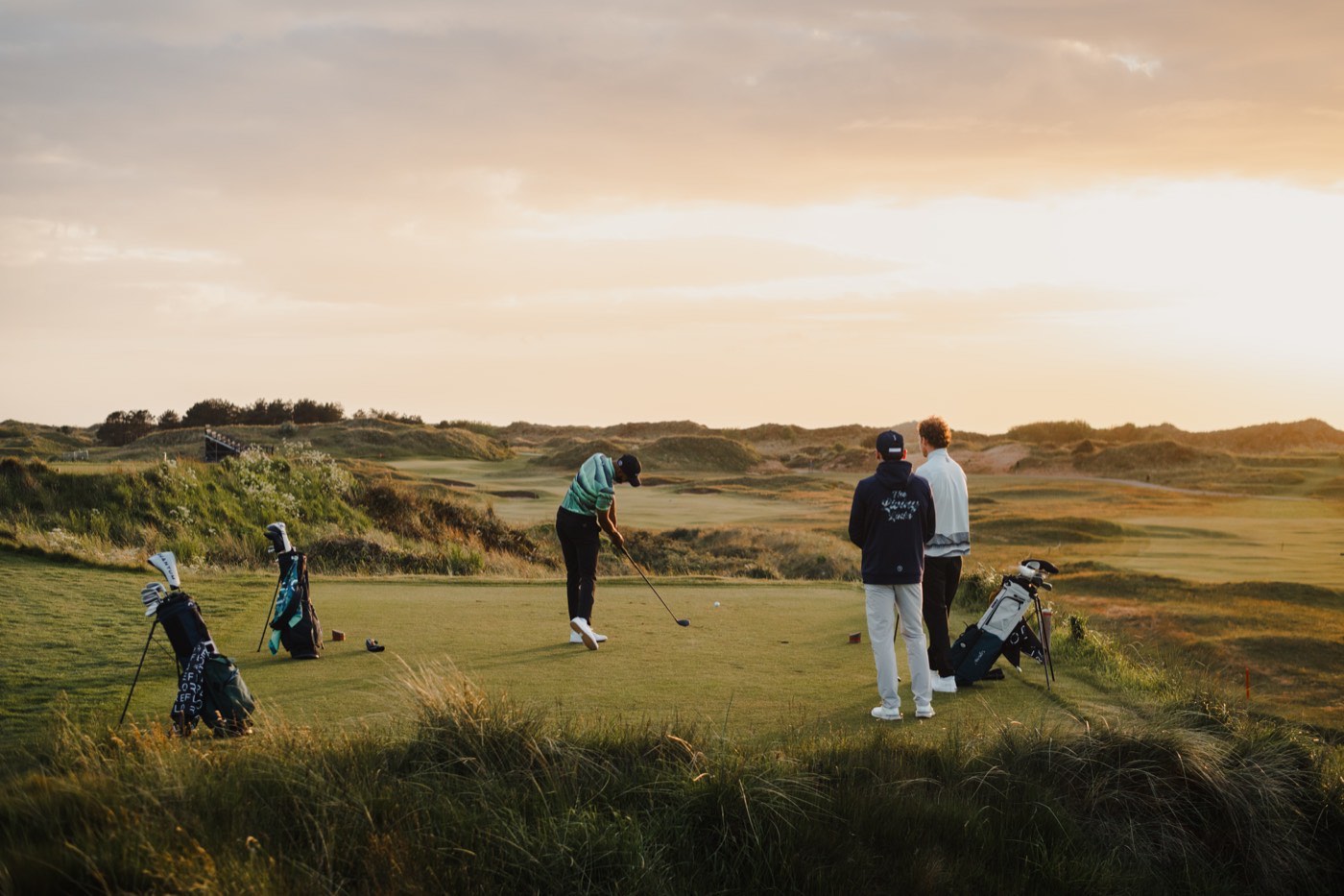 Golfers and caddies walking the links at sunrise, the course running to the horizon